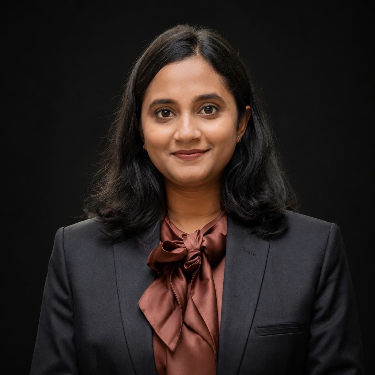 Professional woman in dark suit and brown bow blouse smiling.